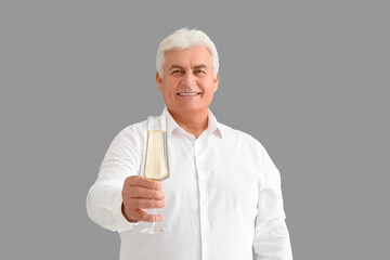 Senior man with glass of champagne celebrating Christmas on grey background