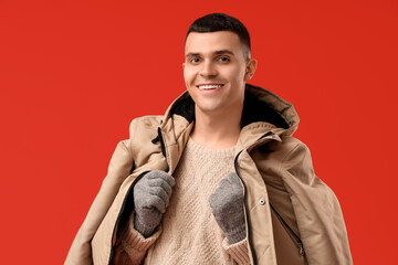 Young man in stylish puffer jacket and gloves on red background