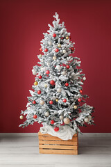 Fir tree decorated with different Christmas balls near color wall