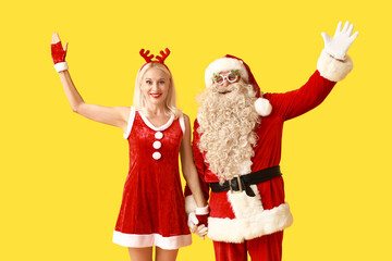 Santa and MRS Claus in Christmas deer horns waving hands on yellow background