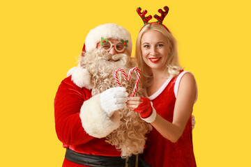 Santa and MRS Claus in Christmas deer horns with candy canes on yellow background
