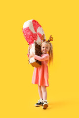Cute little girl in reindeer horns with candy pinata on yellow background