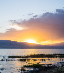 Sunset over calm lake with mountains and dramatic cloudscape in background