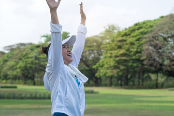 Happy elderly woman raises her hands high up to stretch and twist for exercise in the morning in the park, retirement, senior women exercise