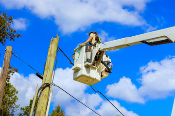 Technician repairs power line pole using hydraulic tower mounted bucket while working on electrical...