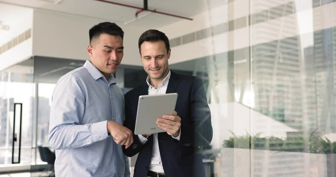 Two multiethnic businessmen collaborating, planning strategy, working together on project, coordinating tasks, allocating resources, monitoring sales results using project management apps on tablet