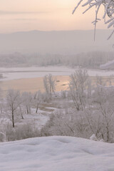 Winter landscape - view across the river to the opposite bank on a foggy winter day and a fisherman on a boat in the distance