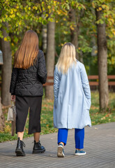 Two women walking in a park, one wearing a black coat