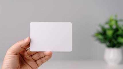 Obraz premium A hand holds a blank white card against a minimalist background with a small potted plant, suggesting themes of creativity, branding, or personal expression.