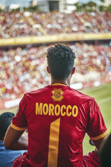 Fototapeta premium Crowd of Moroccan Supporters in Red Jerseys. A vibrant, emotional photo of a crowd of football fans cheering, with one male fan in focus, celebrating Morocco’s success in a packed stadium. 