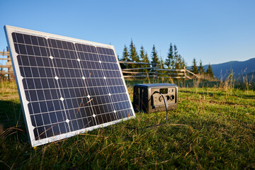 Tourist tent with solar panel and portable power station nearby in grassy field. Scene surrounded...