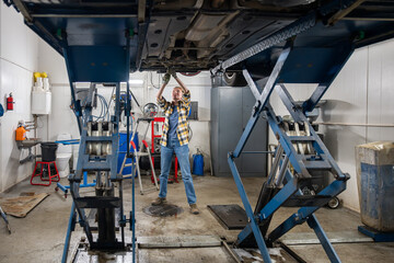 female mechanic standing under lifted car and fixing car in garage
