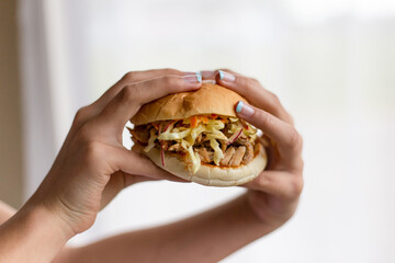 Hands picking up burger with meat and slaw