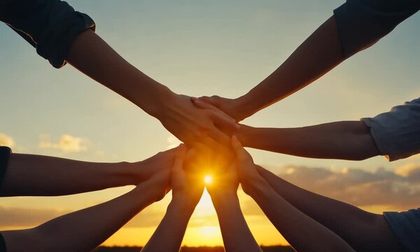 Hands stacked together against a sunset, symbolizing unity and teamwork.