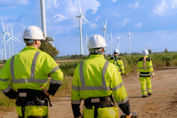 A team of engineers in high visibility safety gear stand together at a wind farm, conducting inspections and discussing renewable energy projects. Wind turbines surround them under a clear sky.