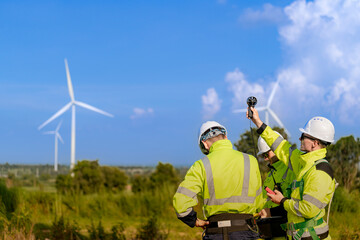 A team of engineers in high visibility safety gear stand together at a wind farm, conducting...