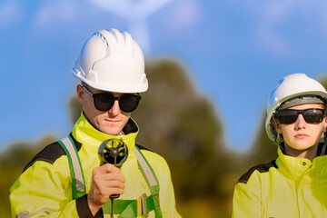 A team of engineers in high visibility safety gear stand together at a wind farm, conducting inspections and discussing renewable energy projects. Wind turbines surround them under a clear sky.