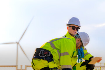 Two engineers wearing high visibility safety jackets and helmets measure wind speed with an...