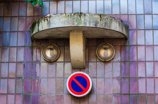 Whimsical Face on Parisian Building: Street Art Meets Urban Architecture. Two vintage spotlights form eyes while a no-parking sign creates an accidental mouth on this quirky building facade in Paris.
