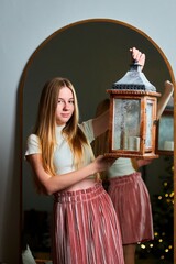 A beautiful young girl stands against the background of a mirror with a flashlight in her hands....