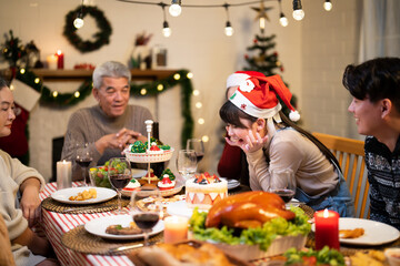 Asian joyful family shares Christmas dinner, surrounded by festive decorations, lights, and traditional holiday foods like grilled turkey and cupcake desserts at cozy home