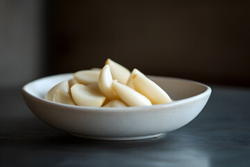 Peeled garlic cloves in a white ceramic bowl on dark table surface, creating a striking contrast and visual balance