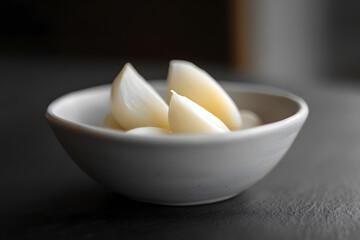 Peeled garlic cloves in simple white ceramic bowl on dark table, emphasizing natural ingredients and clean, modern presentation