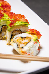 Close up of sushi roll with fried shrimp inside and fresh avocado and salmon on the top