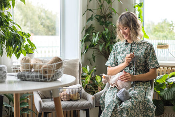 A young beautiful smiling girl crochets from gray yarn and strokes a sphinx cat.