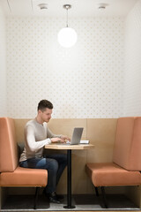 Focused young Caucasian freelancer man working at laptop in office booth, sitting at table, typing. One entrepreneur, business owner, freelance employee using computer at separate rental workplace