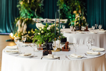 Luxurious restaurant. Luxurious interior, white tables, serving dishes and glasses for guests. Green decor
