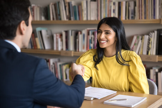 Happy young Indian student girl getting job, shaking hands with male employer in library, entering internship program, smiling, laughing, thanking teacher for educational training course