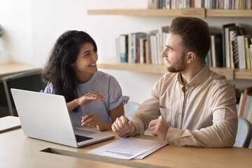 Obraz premium Happy multiethnic colleagues discussing startup marketing strategy, sales reports at workplace table, talking at computer, enjoying teamwork, office friendship, business partners relationships