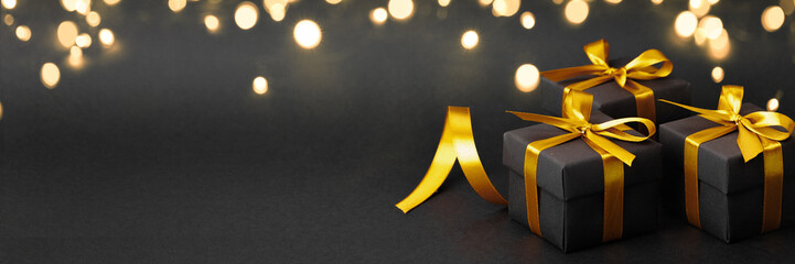 Three elegant black gift boxes with gold ribbons on a black background