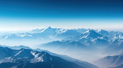 Obraz premium A vast mountain range with snow-capped peaks stretches towards the horizon, with a clear blue sky above.