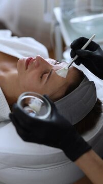 Cosmetologist performs a facial peeling procedure on a young woman.