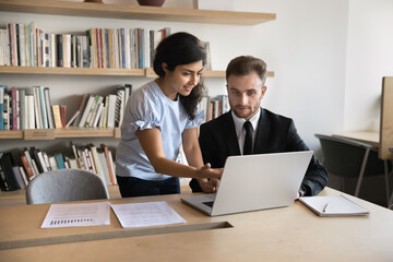 Diverse business colleagues working on marketing strategy at laptop together, talking at workplace. Indian mentor woman showing online project presentation to Intern man