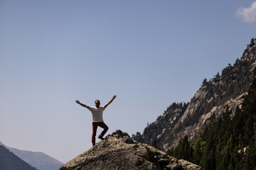 A man is standing on a mountain top, smiling and looking up at the sky