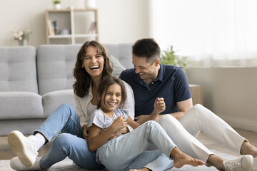Sweet home. Laughing candid millennial spouses with preteen child mother father little daughter...