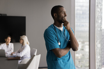 Smiling young male doc working in friendly international team take break from staff conference look...
