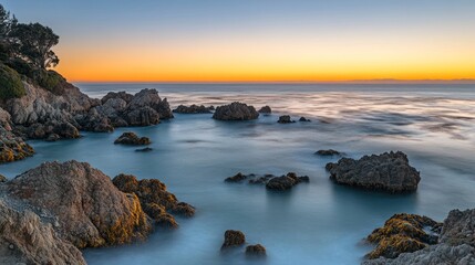 A stunning sunrise over a rocky coastline with the ocean in the background.  The water is calm and the sky is a vibrant orange and pink.