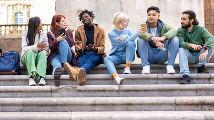 Obraz premium Diverse students relaxing on campus stairs, multicultural friends using smartphones and socializing outdoors