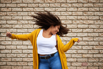 Excited, woman and dancing with hair flip for playful movement, energy and fun celebration of fashion winner. Happy, girl and rhythm for success, freedom and deal achievement on brick wall background
