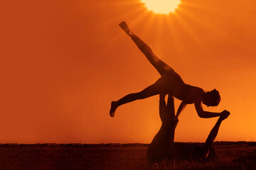 Young couple practicing yoga at sunset. pair doing exercise on green grass. yoga poses in the...