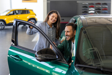 Salesman with financial document talking to client sitting in new car at showroom, man buying a car...