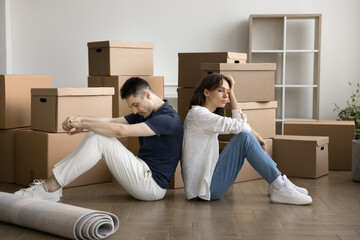 Relocation is hard work. Fatigued exhausted young family couple first time home buyers sit on floor back to back take break rest from carrying boxes unpacking belongings feel too tired at moving day