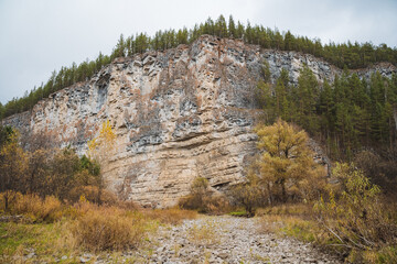 There is a large rocky hill which is situated prominently in the landscape, and it features an abundance of trees flourishing on its summit, creating a beautiful natural scene
