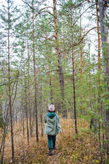 A woman leisurely strolls through a serene and tranquil forest, following a winding path that is beautifully surrounded by lush greenery, vibrant plants, and tall, majestic trees