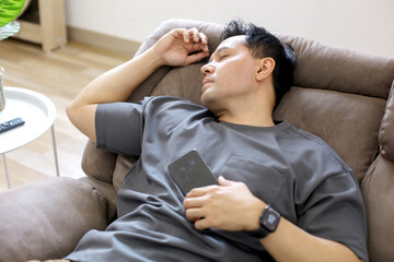 Tired Asian Man Sleep on Sofa After Done Watching TV and Using Phone
