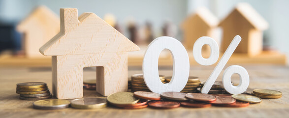 A wooden house model stands beside coins and a "0 percent" sign, symbolizing low mortgage rates or affordable housing options.